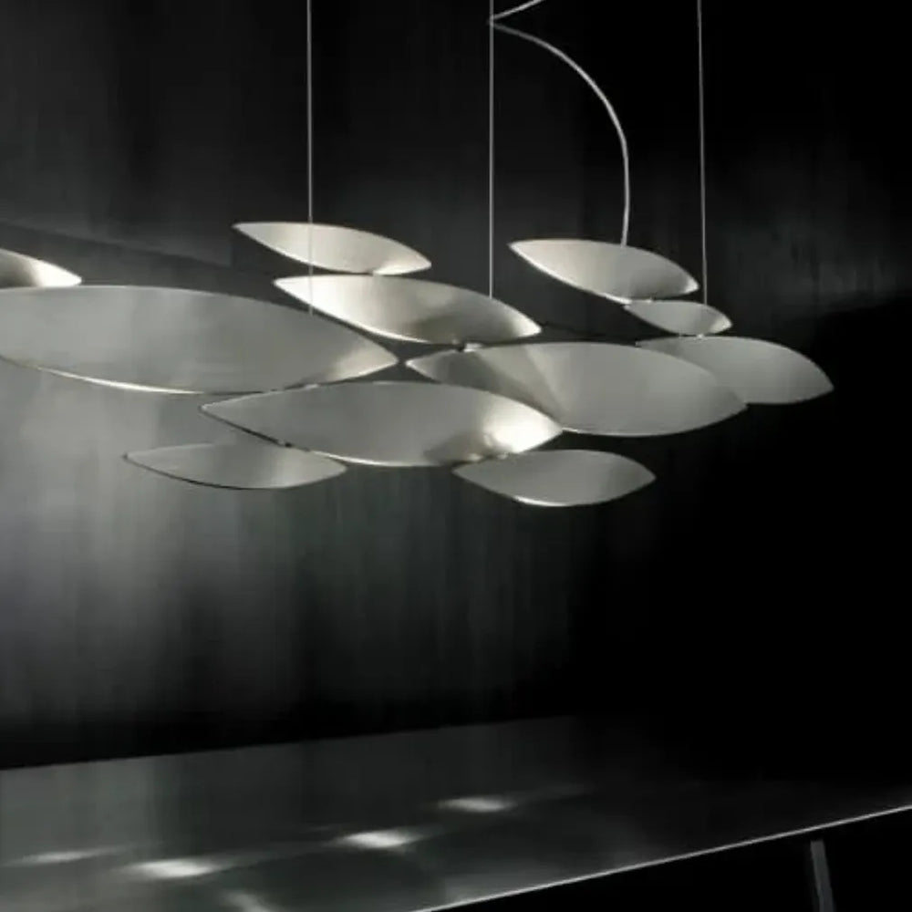 Terzani I Lucci Argentati linear chandelier suspended above a tufted sofa and ottoman against a dark paneled wall.