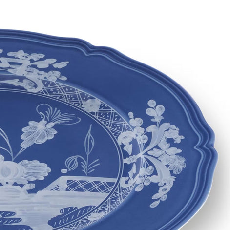 A close-up of a blue ceramic platter with a white floral and botanical pattern, showing the scalloped rim and part of the interior design on a white background.