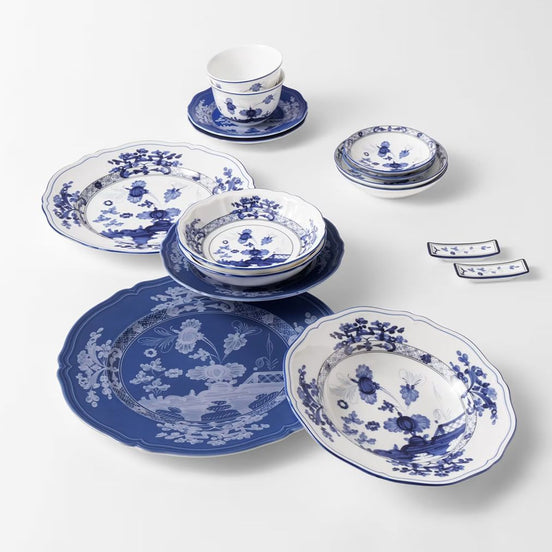 A blue and white porcelain dinnerware set arranged on a light gray background, including plates, bowls, a cup and saucer, stacked dishcloths, and two small napkins.