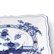 A close-up of a white ceramic plate with a blue floral and botanical pattern, showing the scalloped rim and part of the decorative center design.