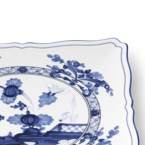 A close-up of a white ceramic plate with a blue floral and botanical pattern, showing the scalloped rim and part of the decorative center design.
