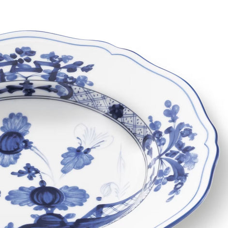 A close-up of a white ceramic plate with a scalloped rim, decorated with blue floral and geometric patterns.