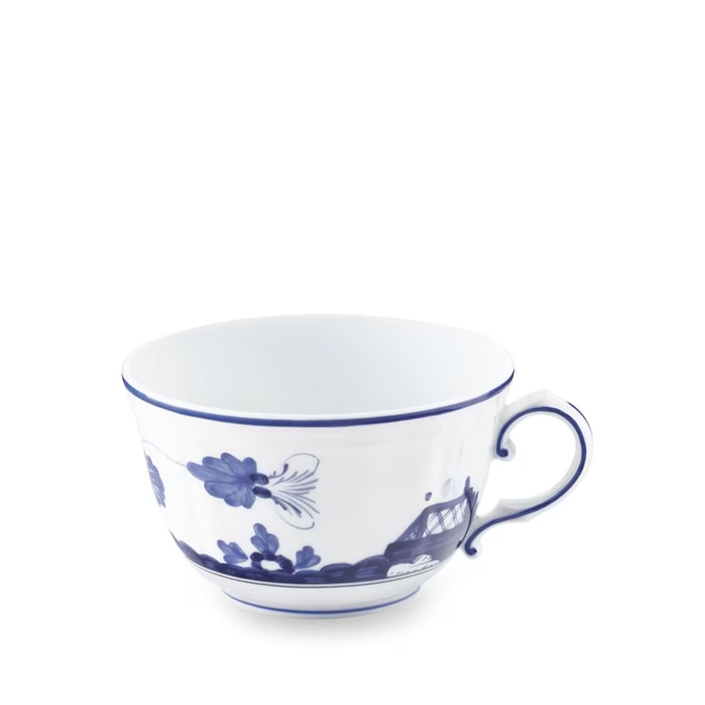 A white porcelain teacup with a blue floral and architectural pattern, featuring a curved handle and a thin blue rim, set against a plain white background.