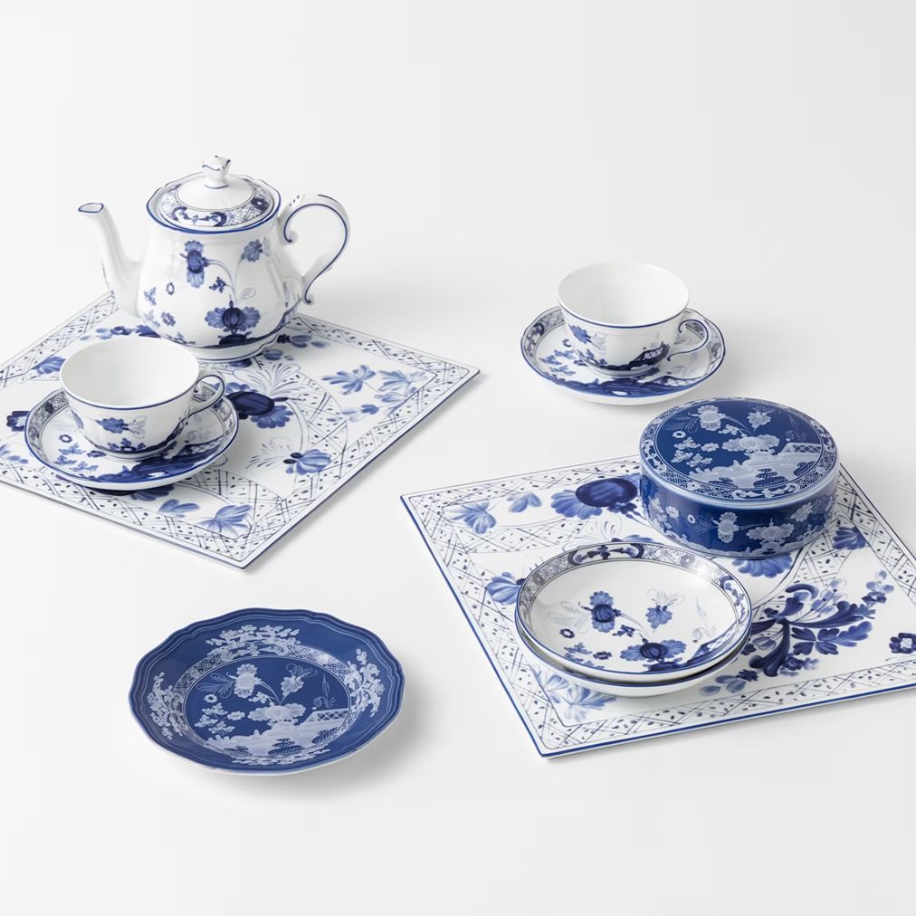 A blue and white porcelain tea set arranged on matching placemats against a clean white background. The set includes a teapot, teacups with saucers, a lidded tea pot, a small bowl, a shallow dish, and stacked plates.