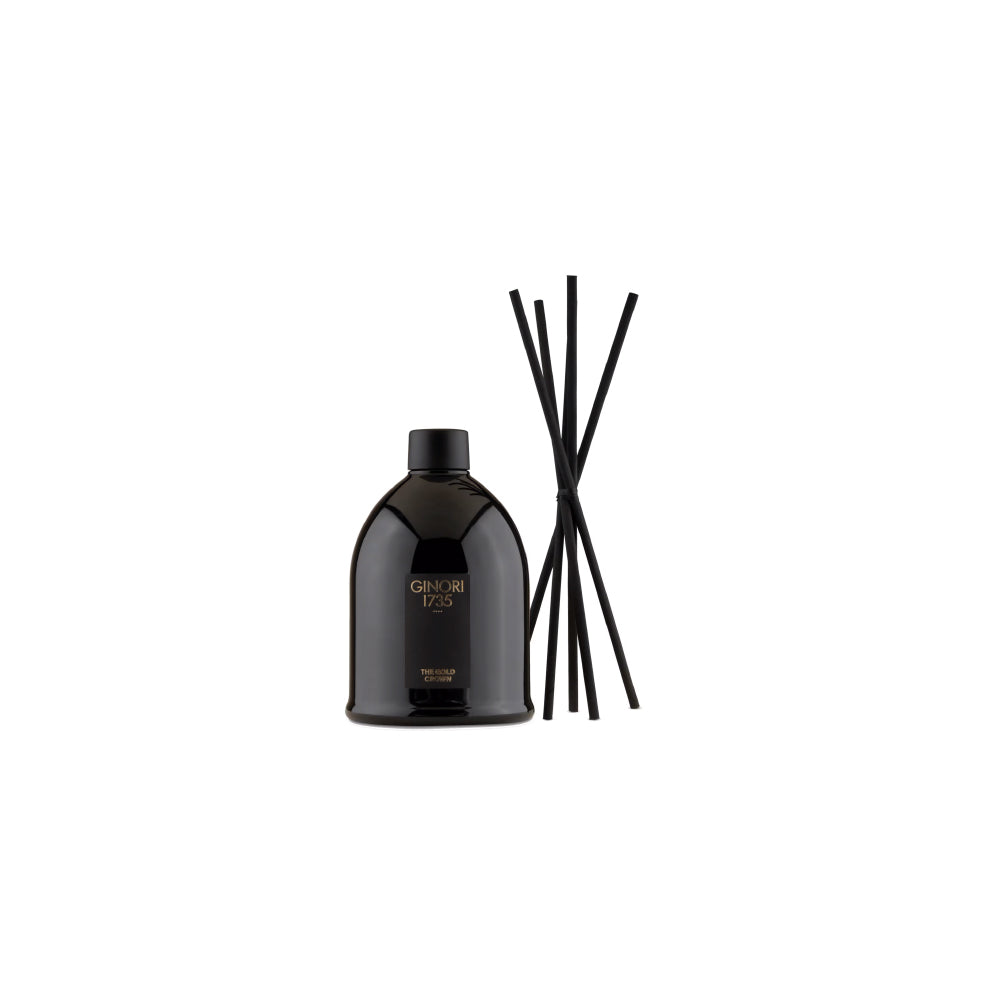 A black reed diffuser bottle with gold lettering next to six black reed sticks, set against a plain white background.