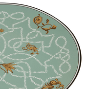 A close-up of a round plate featuring a sage green background with a repeating white 'GINORI' pattern and gold-toned decorative motifs, framed by a thin black rim.