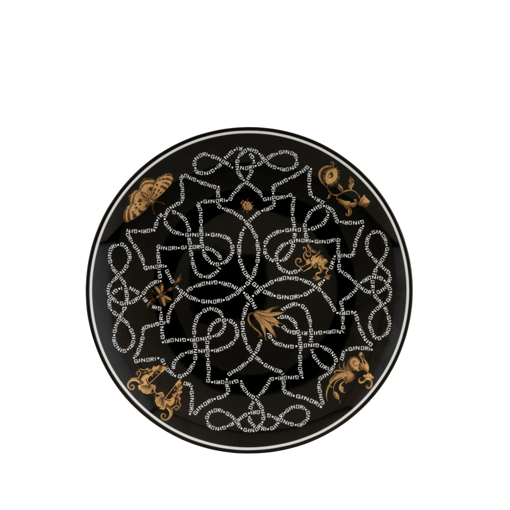 A round black ceramic plate featuring an intricate white dotted geometric knotwork pattern and gold-toned decorative motifs, shown from a top-down view on a white background.