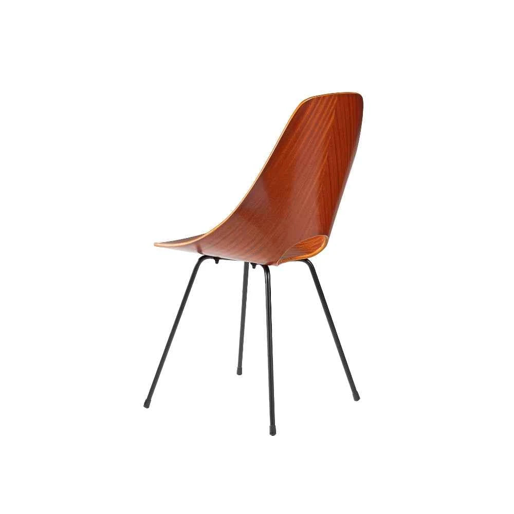 An icon of twentieth-century design, the Sedia Medea is defined by a single continuous shell in moulded plywood with a glossy mahogany veneer — a fluid, ergonomic curve pierced by the signature handle-like opening that lends the chair its unmistakable identity. The sculptural shell rests upon a slender matt-black painted iron structure, grounded by discreet black rubber pads, while four golden studs on the seat provide an exquisite detail of refined ornamentation. Noble materials including wood and metal ar