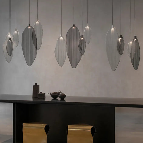 Multiple Terzani Harpe pendants in silver and dark tones suspended above a dark counter with gold-tone stools.