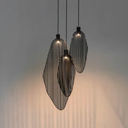 Three dark-tone Terzani Harpe pendants at staggered heights, casting warm light and vertical shadows on a gray wall.