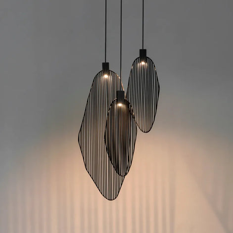Three dark-tone Terzani Harpe pendants at staggered heights, casting warm light and vertical shadows on a gray wall.