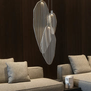 Three illuminated silver-tone Terzani Harpe pendants hanging above upholstered seating against a dark living-room wall.