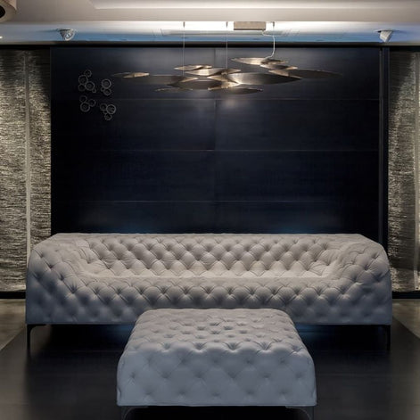 Terzani I Lucci Argentati linear chandelier in a bright living room above white seating, with overlapping sculptural elements and soft downward illumination.
