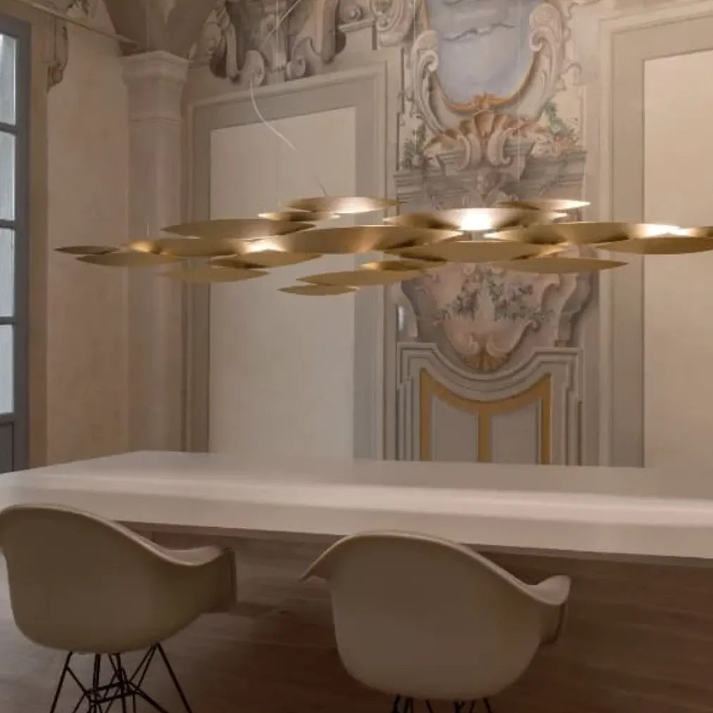 Terzani I Lucci Argentati linear chandelier above a glass dining table in a contemporary kitchen, showing its flowing fish-inspired silhouette.