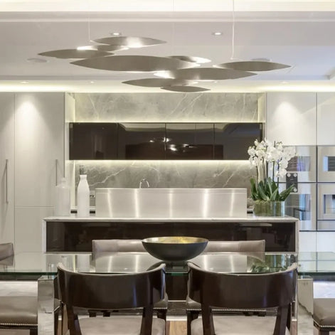 Silver-tone Terzani I Lucci Argentati chandelier suspended above a dark table, casting pools of downward light from its fish-inspired elements.