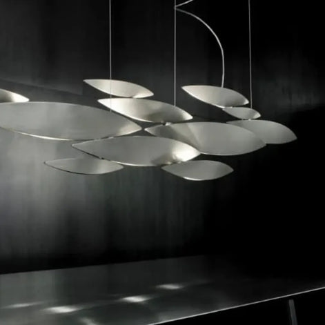Terzani I Lucci Argentati linear chandelier suspended above a tufted sofa and ottoman against a dark paneled wall.