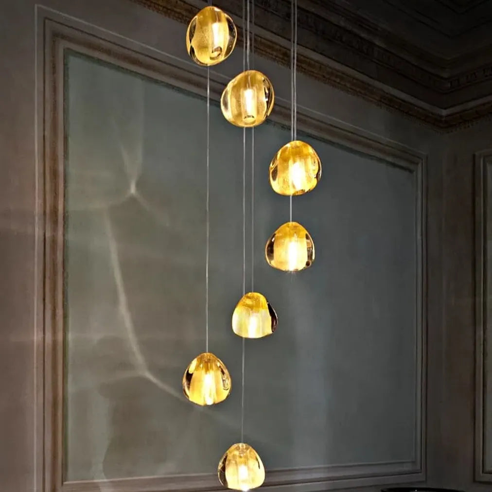 Terzani Mizu 7 pendant light with seven clear, water-drop-shaped crystal shades at staggered heights, casting flowing light patterns on a pale wall.