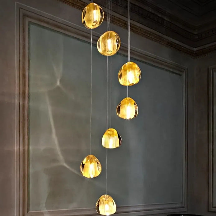 Terzani Mizu 7 pendant light with seven clear, water-drop-shaped crystal shades at staggered heights, casting flowing light patterns on a pale wall.