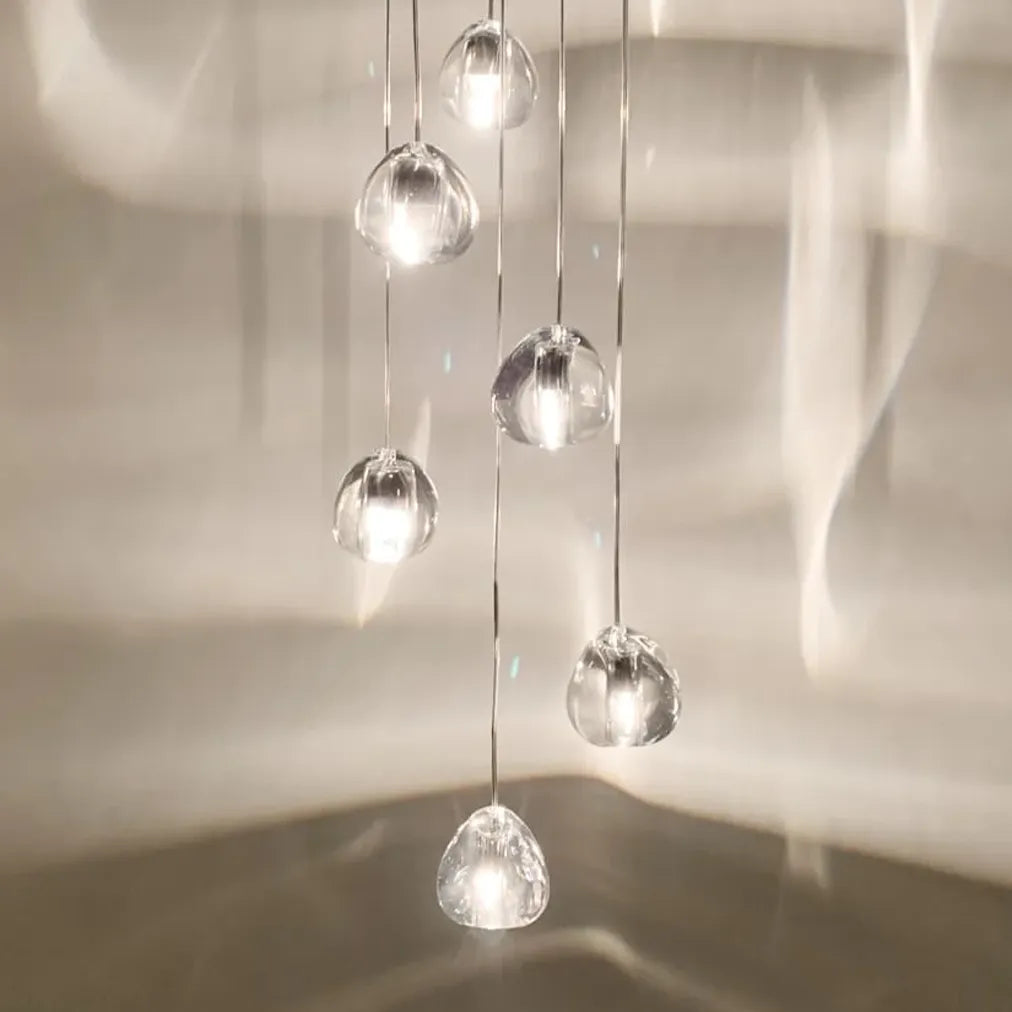 Seven gold-tone crystal shades of a Terzani Mizu pendant arrangement glowing at staggered heights against a paneled wall.