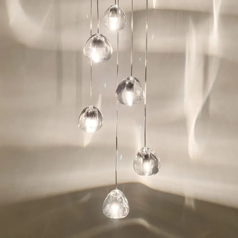 Seven gold-tone crystal shades of a Terzani Mizu pendant arrangement glowing at staggered heights against a paneled wall.