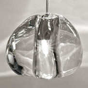 Illuminated Terzani Mizu crystal pendants beside a bed, casting bright, water-like light patterns across a pale paneled wall.