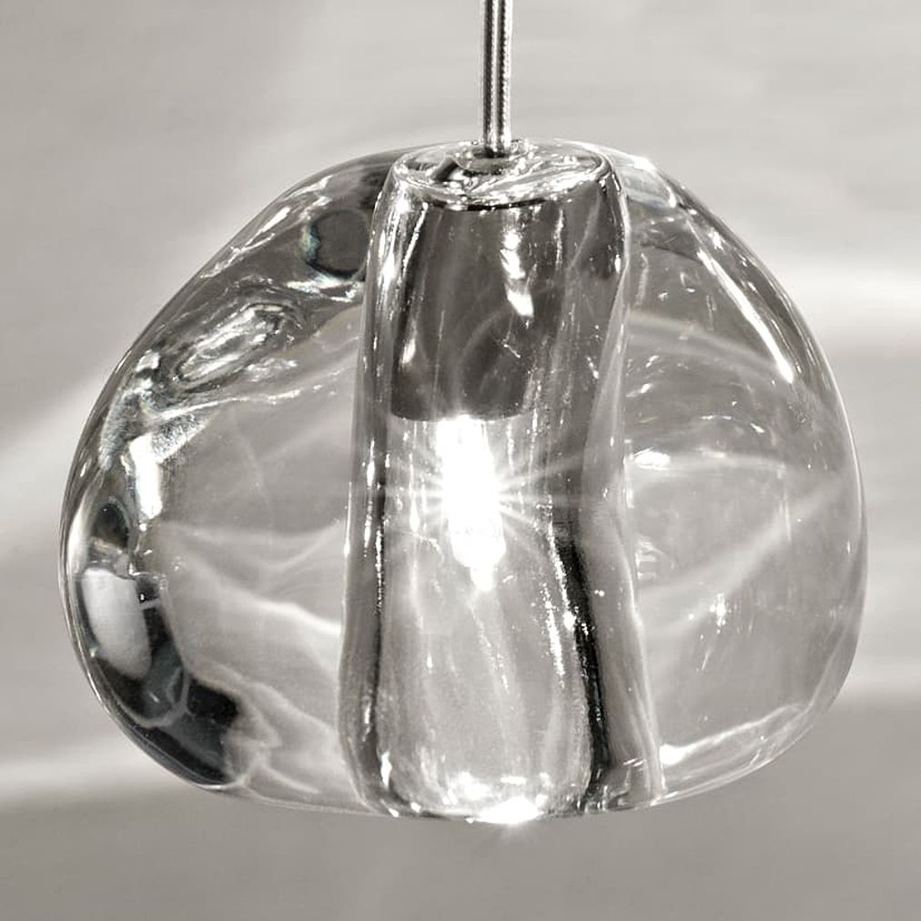 Illuminated Terzani Mizu crystal pendants beside a bed, casting bright, water-like light patterns across a pale paneled wall.