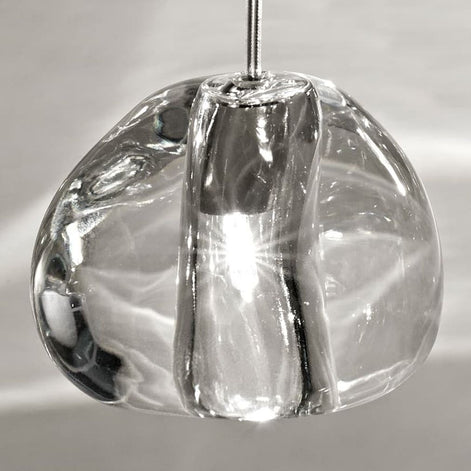 Illuminated Terzani Mizu crystal pendants beside a bed, casting bright, water-like light patterns across a pale paneled wall.