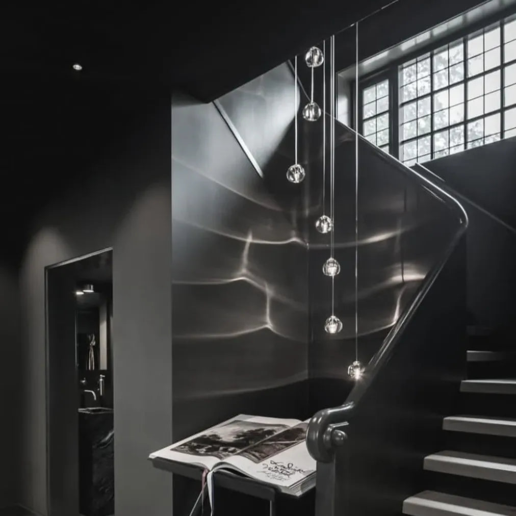 Detail of clear Terzani Mizu crystal pendants hanging at varied heights, with illuminated organic shades and flowing reflections on the surrounding walls.
