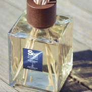 A reed diffuser bottle with a square clear glass container, pale liquid, visible reeds, a dark brown wooden stopper, and a blue label reading 'Salone Nautico Blue Essence' by Euthalia Fragrances.