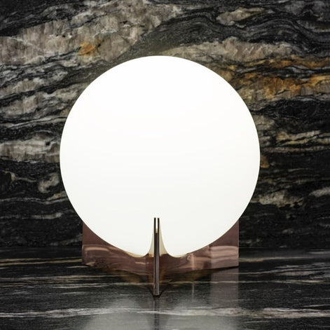 Illuminated Terzani Oscar table lamp with a reflective warm-metal base on a dark veined marble surface.