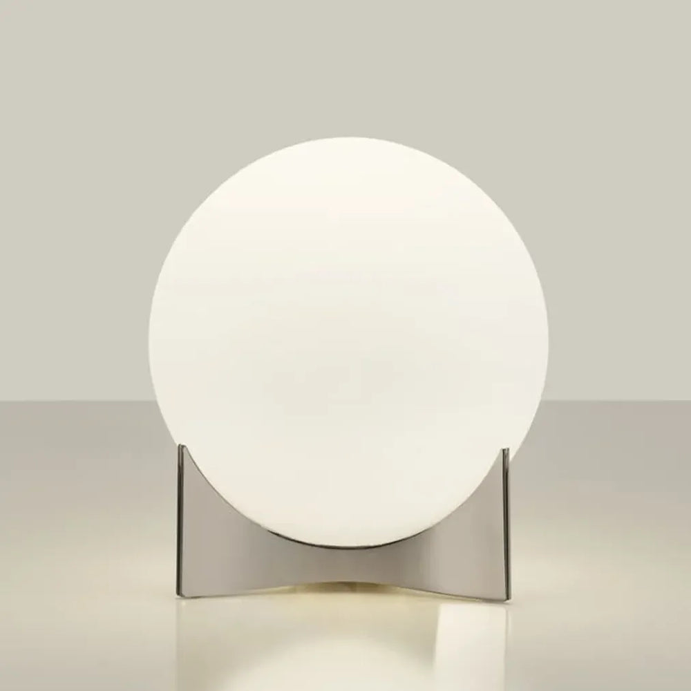 Angled view of the Terzani Oscar table lamp showing its glowing opal glass globe and sculptural silver-tone base on a light background.