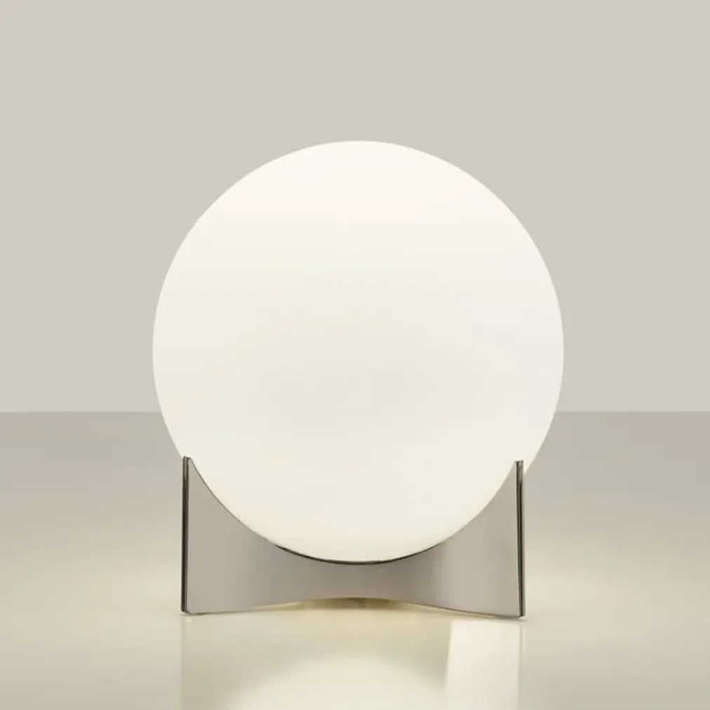 Angled view of the Terzani Oscar table lamp showing its glowing opal glass globe and sculptural silver-tone base on a light background.