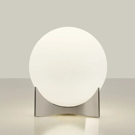 Angled view of the Terzani Oscar table lamp showing its glowing opal glass globe and sculptural silver-tone base on a light background.